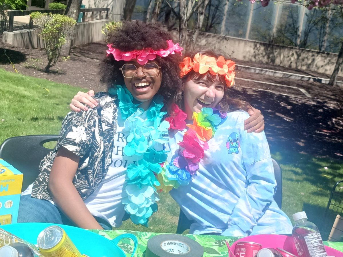 Students Harper Syres, left, and Rachel Bihlmeyer, right, represented ICE News and gave out ICE water drinks from its Hawaiian-themed table during Spring Fling April 30.